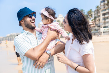 Young indian father and mother playing with their cute little daughter and enjoying summer vacation on tropical beach. Happy family Concept.