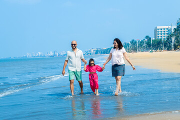 Happy indian Family of three enjoying summer vacation on tropical beach. father and mother holding hands of their daughter. friendly family Concept.