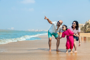 Happy indian Family enjoying summer vacation on tropical beach. father point aside with mother and daughter looking. friendly family Concept.