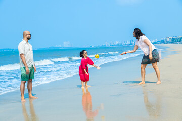 Happy indian Family of three playing with football and enjoying summer vacation on tropical beach. friendly family Concept.