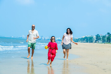 Happy indian Family of three playing and enjoying summer vacation on tropical beach. friendly...