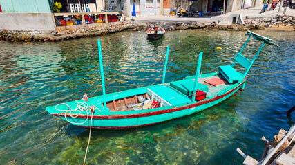 Brightly painted traditional wooden fishing boat moored in clear tropical waters near a coastal village