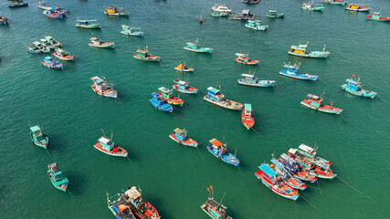 Fototapeta na wymiar Aerial view of a colorful fleet of fishing boats clustered in calm turquoise waters, likely in a coastal fishing village
