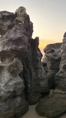 Imposing rock formations on a sandy beach with a soft glow of sunset in the background