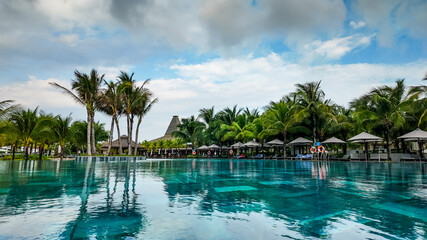 A tranquil resort swimming pool surrounded by palm trees and sun loungers under a clear sky, ideal...