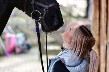 Girl blonde in blue quilted vest with ponytail plays with her horse, portraits of the woman with...