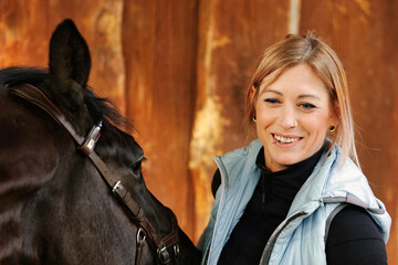 Girl blonde in blue quilted vest with ponytail plays with her horse, portraits of the woman with...