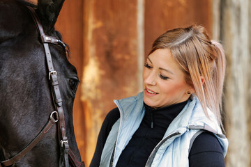 Girl blonde in blue quilted vest with ponytail plays with her horse, portraits of the woman with...