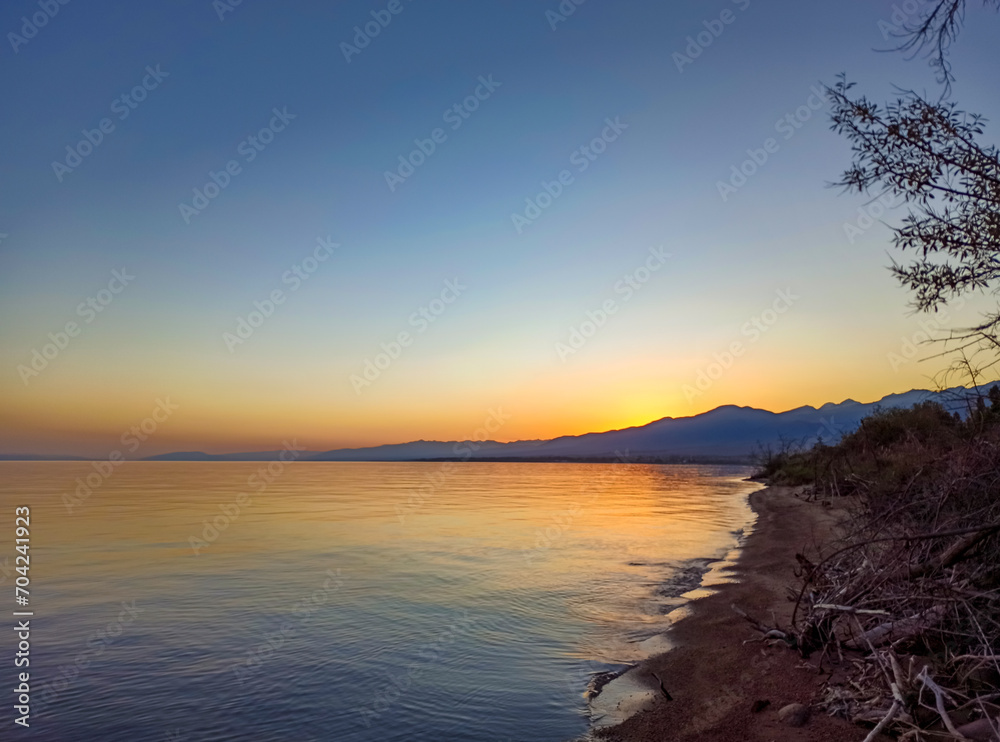 Wall mural Colorful sunset on the sea. Mountain lake in the rays of the orange sun. Kyrgyzstan, Lake Issyk-Kul. natural background