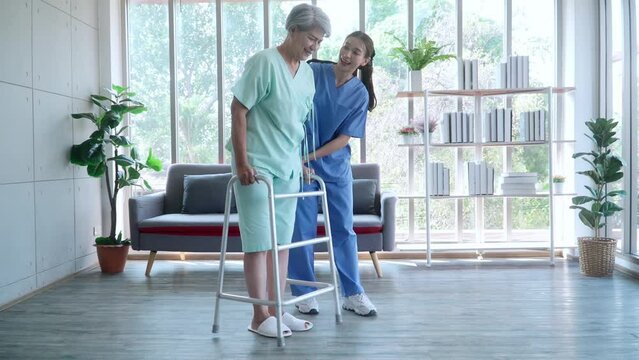 A nurse helping an elderly patient walks by using a walker.