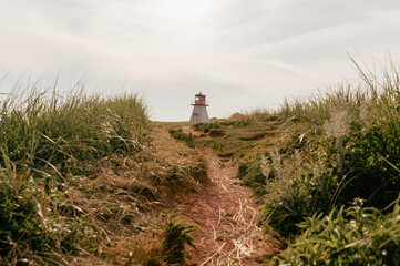 vue sur un phare rouge et blanc avec du gazon vert en été et un chemin en avant plan