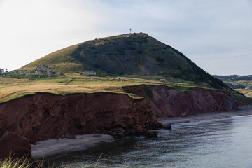 vue sur une colline recouverte de gazon vert avec une falaise à roche rouge en bord de mer lors d'une journée d'été