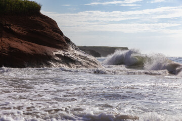 vue sur des vagues qui se frappent au rocher rouge d'été lors d'une journée ensoleillée