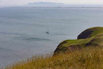 vue sur un bateau à voile avec les voiles baissés sur l'eau vue de la terre avec du gazon vert en été avec une montagne au loin