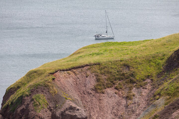 vue sur un bateau à voile avec les voiles baissés sur l'eau vue de la terre avec du gazon vert en été