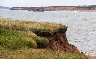 vue sur une falaise en roche rouge au bord de la mer avec du gazon vert sur le dessus en été lors d'une journée ensoleillée