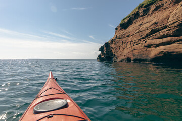 vue sur le bout d'un kayak de mer orange sur l'eau avec une falaise en avant