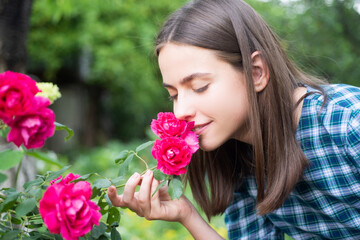 Naklejka premium Beautiful girl smelling a rose flower in spring park. Young woman in flowering garden with roses. Beauty model with spring flowers. Happy spring. Pretty woman enjoying smell flowers in spring park.
