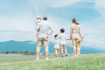 家族旅行・青空の見える公園で遊ぶ家族・ファミリー・親子の後ろ姿
