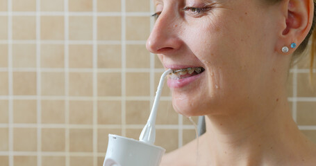 Young woman cleaning her teeth with brace by oral irrigator.