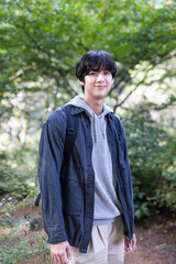 Portrait of an Asian Korean handsome young man wearing a dark gray T-shirt standing in the forest looking at the camera and smiling