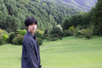 Portrait of an Asian Korean handsome young man in a dark gray T-shirt smiling at the camera while standing in a green field, a copy space