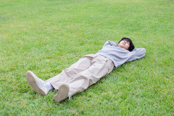 A young man lies down on a green lawn in an outdoor park on a sunny day and relaxes - Powered by Adobe