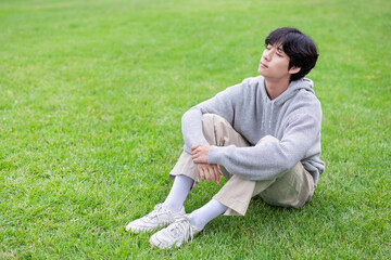 A young man sits on a green lawn in an outdoor park and relaxes during the sunny day
