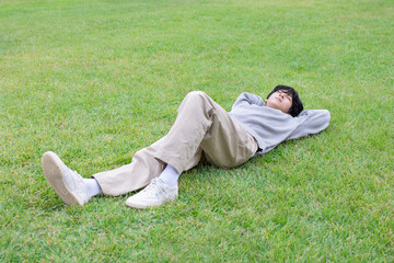 젊은 청년 한명의 남자가 화창한 낮에 야외 공원 초록 잔디 밭에 누워서 휴식하며 여유을 즐기고 있다
