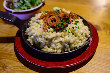Pongauer Kasnocken Cheese Spaetzle Pasta in an Iron Pan with Fried Crispy Onion and Green Salad