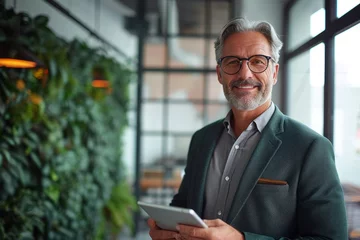 Fotobehang Smiling middle aged business man ceo investor using tablet computer, mature older businessman executive looking at camera advertising finance trading work standing in office. Generative AI  © Ashutosh