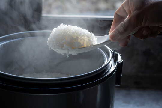 Jasmine rice cooking in electric rice cooker with steam on dark background. Soft Focus,
