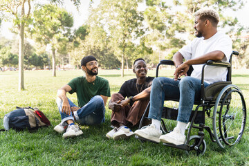 University Student on wheelchair together with young friends talking sitting on campus park grass