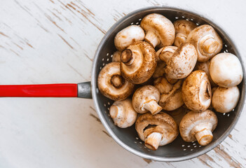 Raw mushrooms in an iron bowl on a white wooden background