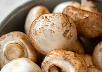 Raw mushrooms in an iron bowl on a white wooden background