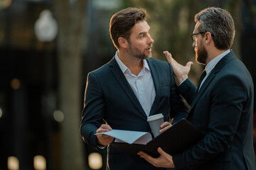 Photo of business partners talk conversation outdoor. Two handsome businessmen in suits discuss a...
