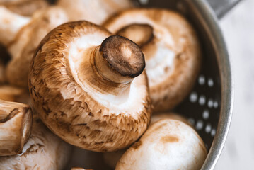 Raw mushrooms in an iron bowl on a white wooden background
