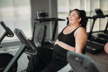 Plus size Asian woman exercises in gym. Beautiful overweight woman in sportswear doing cardio...