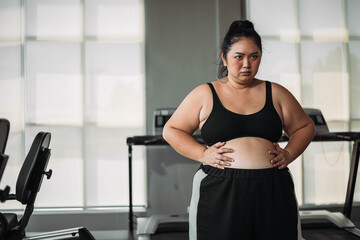 Plus size Asian woman exercises in gym. Beautiful overweight woman in sportswear serious about fat...