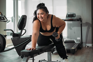 Plus size Asian woman exercises in gym. Beautiful overweight woman in sportswear doing workout in...
