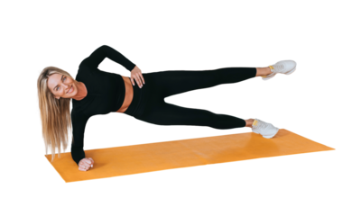 Attractive caucasian blonde woman in black sportswear makes plank exercise looks at camera happy smiles against transparent background. American fitness model training at gym. Endurance
