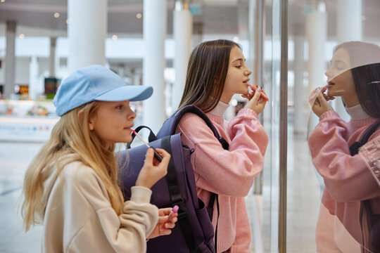 Beautiful girls doing makeup with lipstick looking at store window at mall
