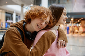 Portrait of loving teenage couple hugging while spending time at shopping mall