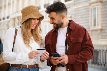 Young Caucasian couple buying the tour tickets with credit card and phone to visit Madrid, Spain. - obrazy, fototapety, plakaty