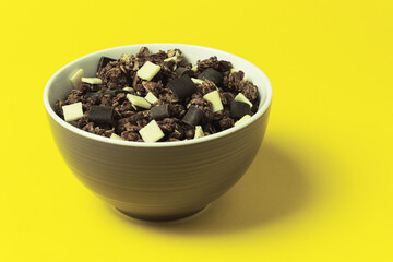 Granola with oatmeal and chocolate chips in a clay glazed bowl on a yellow background