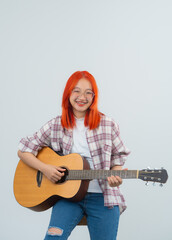 Smart asian woman red hair and wearing glasses musician play guitar on grey or white background....