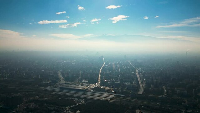 Aerial drone shot of the cityscape of the capital of Bulgaria - Sofia. Sunny blue sky foggy view towards the Vitosha mountain with the city center in the foreground. Misty footage of the skyline.
