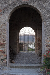 Time-Worn Charm: A vintage stone archway and weathered brick walls frame a closed metal gate, offering a glimpse into a blurred, historic landscape