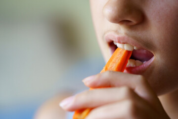 Anonymous teenage girl biting carrot slice at home