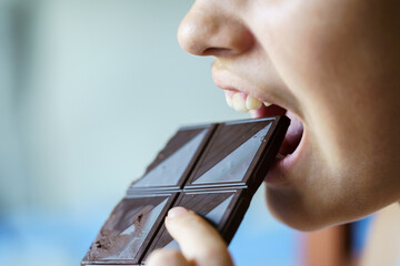 Anonymous girl with mouth open eating chocolate bar at home